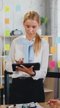 Sevimli gülümseyen, deneyimli, iş yerinin yanında tabletle duran, çok kültürlü kadın ortakların sorumluluğunu üstlenen ve ortak iş stratejisinde fikirlerini paylaşan sarışın bir kadın.