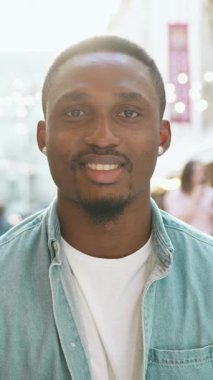 Yakışıklı, gülümseyen, 30 yaşında, modaya uygun, koyu tenli, yuvarlak küpeli ve bakımlı sakallı bir adam. Açık hava kafeteryasında kokteyl içerken kameraya poz veriyor.