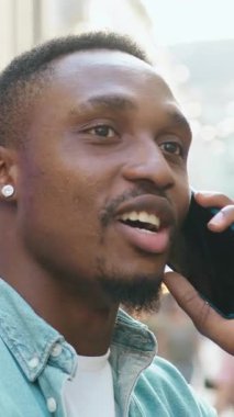 Sevimli, 30 yaşında, modern, sakallı Afrikalı Amerikalı kulaklarında yuvarlak küçük küpelerle şehir merkezinin ortasında açık büfelerle dikilirken cep telefonuyla konuşuyor.