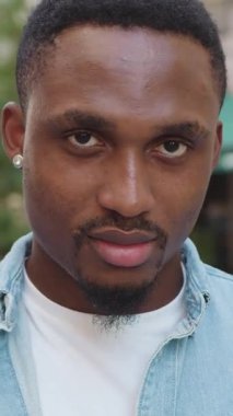 Çekici bir ruh hali var. Afrikalı Amerikalı genç bir adam günlük giysiler içinde küçük küpeler takıyor. Yazın açık hava kafesinin arka planında kameranın önünde duruyor.