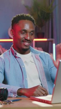 Güzel görünümlü, neşeli, 30 'lu yaşlarda, rahat, Afro-Amerikan' ın dizüstü bilgisayarın yanında oturduğu ve renkli ışıklandırma geçmişi olan rahat odada arkadaşlarıyla keyifli bir video konuşması yaptığı bir yer.