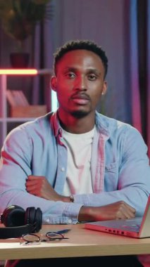 Güzel dekore edilmiş ev ofisinde kameraya 30 yaşında, konsantre olmuş Afro-Amerikan pozları ve dizüstü bilgisayarı üzerinde çalıştığı süre boyunca gece ışıkları.