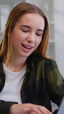 Çekici, güler yüzlü, modern sarışın kadın evdeki masada oturmuş arkadaşlarıyla bilgisayar başında sohbet ediyor. Yavaş çekim.