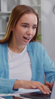 Ev ofisinden dizüstü bilgisayarda çalışan genç ve serbest çalışan bir kadın. Laptop ekranına bakan kız e-postada iyi haberleri okuyor iyi haberleri kutlarken eğleniyor. Yavaş çekim.