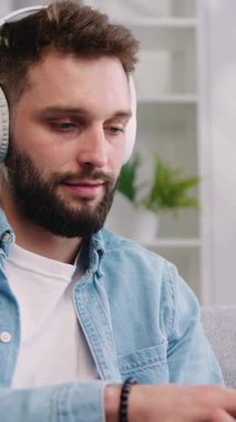 İyi görünümlü, kendine güvenen, kulaklıklı, evdeki kanepede oturan ve dizüstü bilgisayarla çalışan akıllı bir adam. Erkek serbest yazar ya da öğrenci evde çevrimiçi bir konferans dinliyor. Yavaş çekim.