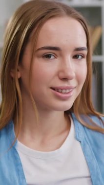 Çekici, mutlu, genç bir kadın evdeki rahat koltukta oturuyor ve kameraya gülümseyen, tatmin olmuş bir yüz ifadesiyle bakıyor, kadın portresi. Yavaş çekim.