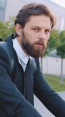 Sevimli, kendine güvenen, 30 yaşında, bakımlı sakallı, güzel, büyük şehir binasının yanında yeşil ağaçlı bisiklete binen bir ofis çalışanı.