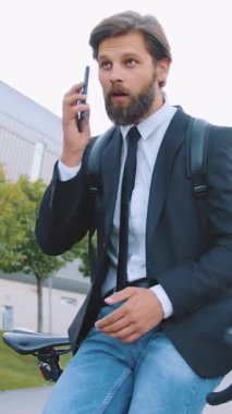 Çekici, zeki, deneyimli, 30 yaşında, iş ceketi ve kot pantolonuyla şık sakallı bir ofis çalışanı. Bisikletinin üstünde oturuyor ve etkileyici bir binanın yakınında, hareketli bir konuşma yapıyor. Kapatın.