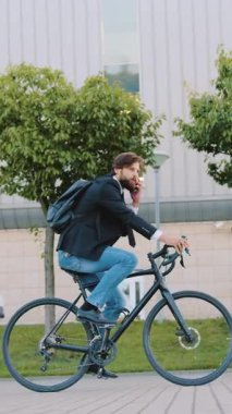 Keyifli, keyifli, 30 'lu yaşlarda sakallı bir adamın yan görünüşü. Yanında yeşil ekili, büyük bir inşaatta bisiklet sürerken keyifli, hareketli bir sohbeti var.