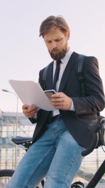 Yakışıklı, kendine güveni tam, 30 yaşında, bakımlı sakallı, resmi kıyafetleri olan, modern cam binanın yakınındaki bisikletine yaslanmış bir iş adamı.