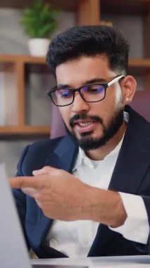 Modern ofisinde oturan resmi takım elbiseli yakışıklı Hintli sakallı iş adamı online bir ders veriyor, müşterilerine dizüstü bilgisayar kullanmalarını tavsiye ediyor. Yavaş çekim