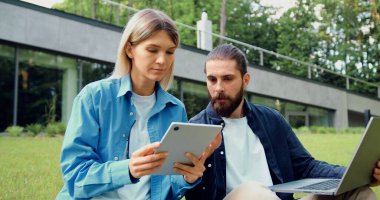 Dışarıdaki çimlerin üzerinde oturan iki meslektaşım bir dizüstü bilgisayar ve tabletle iş birliği yapıyorlar. Adam kadına bir şey anlatıyor, tabletindeki ekranı işaret ederek birlikte çalıştıklarını gösteriyor..