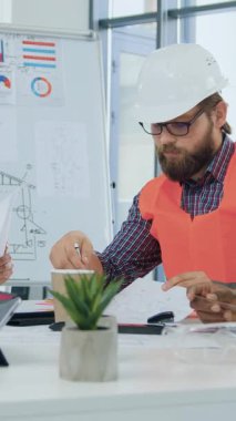 İnşaat endüstrisinde deneyimli deneyimli erkek ve kadın uzmanlar toplantı odasında toplanıyor ve bina projesinin detaylarını tartışıyorlar, bina planlarını gözden geçiriyorlar.