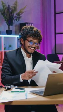 İş zaferi konsepti. Çekici, yüksek yetenekli, kıvırcık sakallı, gözlüklü Müslüman iş adamı. Bir sürü belge kusuyor ve çalışma odasında dans ederken harika duygulardan keyif alıyor.