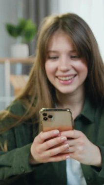 Çekimi hızlandıran, çekici, mutlu, 25 yaşında bir kadın. Telefonunu kullanarak başarılı bir şekilde verilen sonuçları okuyor ve zevkten dört köşe oluyor.