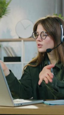 Uzaktan çalışma konsepti. 25 yaşında, çekici, duygusal, kablosuz kulaklıklı bir kız çalışanın ev bilgisayarındaki bilgisayar konferansında meslektaşlarıyla konuşması.