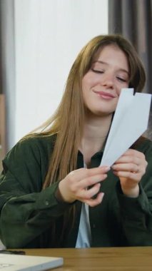 Sevimli, mutlu, neşeli, 25 yaşında, kahverengi saçlı kadın ofis masasında kameranın önünde oturuyor ve el yapımı kağıt uçak fırlatıyor.