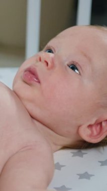 İki aylık güzel bir erkek bebeğe karın masajı yapan kadınların ellerini kapatıyoruz. Küçük bebek beyaz karyolada yatarken annesi onu nazikçe sağlıklı jimnastik yapıyor. Sağlıklı bebek kavramı. Yavaş çekim