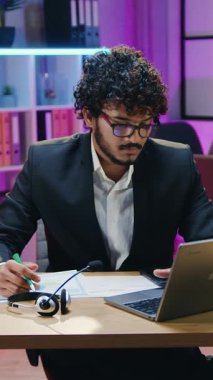 Yakışıklı, kıvırcık sakallı, Müslüman iş adamı ve geleneksel tesettürlü kadın iş arkadaşı, gece yarısı bilgisayar başında partnerlerle video konferansı sırasında çalışma odasını aydınlatıyor ve raporları çizelgelerle tartışıyor.