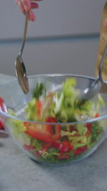 Bilinmeyen bir kadının kırmızı biber, marul, salatalık ve kiraz domateslerini cam kasede karıştırıp taze vitamin salatası hazırladığı ev yapımı hazırlık konsepti.