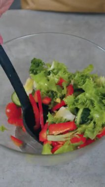 Kimliği belirsiz bir kadının mutfak masasının yanında durup besleyici vitamin sebze salatasıyla zeytinyağını karıştırdığı ev yapımı beslenme konsepti.