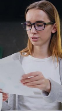 Bilgisayarda çalışan, ev yazımında kağıt hesapları okuyan, kağıtlara notlar yazan, gülümseyen, odaklanmış iş kadını bir bayan öğrenci. Dairesinde çalışan serbest çalışan biri. Yavaş çekim.