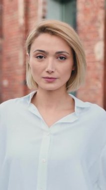 Beyaz gömlekli güzel beyaz kadın portresi. Gün içinde şehir merkezinde kameraya gülümsüyor. Dışarıdaki kameraya bakan neşeli, pozitif bayan.