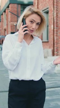 Beyaz gömlekli başarılı bir iş kadını şehir merkezinde cep telefonuyla konuşuyor. Güzel genç bir kadın sokakta cep telefonuyla konuşuyor. Telefon konuşması yapan serbest çalışan bir kadın. Yavaş çekim