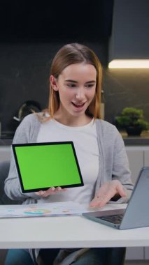 Laptop kullanan çekici bir kız video konferansı düzenliyor. Kadın, çağrı video konferansı sırasında yeşil ekranlı tablet gösteriyor. Krom anahtar teknolojisi, pazarlama tasarım konsepti. Yavaş çekim.