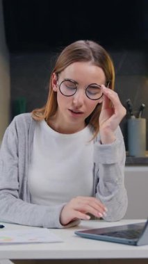 Dizüstü bilgisayarda oturan genç bir kadın baş ağrısını hafifletmek için gözlüğünü çıkarıp şakaklarına masaj yapıyor. Yorgun kız öğrenci evde online işe kısa bir ara veriyor. Stresli bir migren sorunu. Yavaş çekim.