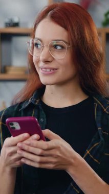 Gülümseyen kadın uzaktan kumandalı akıllı telefon kullanarak şık bir oturma odasında kanepede oturuyor. Sanal ev ofisi, uzak mesafe işi. Serbest Çalışan. Yavaş çekim.
