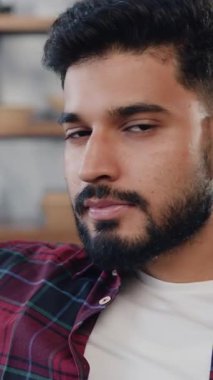 Yakın plan. Portre astarı rahat koltukta rahatlayıp kameraya bakan mutlu görünüyor. Mutlu Hintli erkek kanepede oturuyor ve kameraya bakıyor..