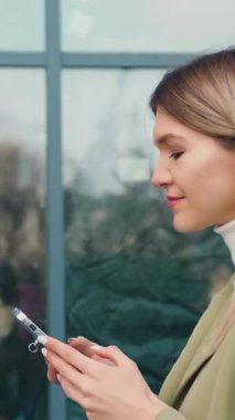 Yakın plan başarılı kadın akıllı telefonuyla sokakta yürüyor ve akıllı telefon kullanarak arkadaşlarıyla sohbet ediyor. İletişim, sosyal ağlar, online alışveriş konsepti. Yavaş çekim.