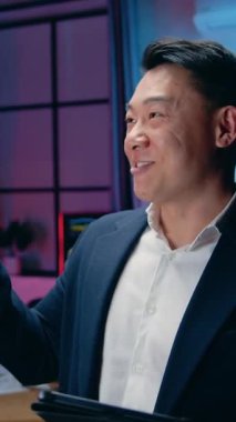 Güzel görünümlü, neşeli, deneyimli erkek ofis müdürü tablet cihazıyla ilgili harika haberlerden keyif alıyor, çalışma odasındaki cam tahtada gece lambalarıyla çalışıyor.