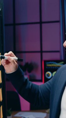 Yakışıklı, yüksek yetenekli, kendine güvenen Asyalı erkek ofis müdürü gece çalışma odasındaki başarısından keyif alıyor, cam duvar ve tablet cihazındaki detayları gözden geçiriyor ve keyifli duygular hissediyor.