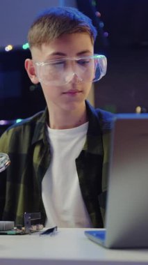 Koruyucu gözlüklü çocuk lehimleme paneli ile lehimleme demiri kullanıyor akşam evde dizüstü bilgisayardaki eğitim videosu sırasında.