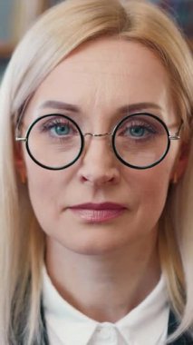 İyi donanımlı bir ofiste gözlüğünü çıkarırken kameraya bakan başarılı yetişkin kadın ofis müdürünün iş portresi.