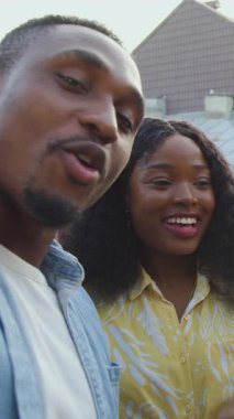 İyi görünümlü neşeli 25 'likler karışık ırk erkekleri ve kızlar birlikte eğleniyorlar, bira ve şarap içiyorlar ve balkondaki akıllı telefonda fotoğraf çekiyorlar şehrin çatılarına bakıyorlar, kapatıyorlar.