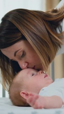 close up of young mother hugging and kissing her adorable few month baby resting in crib and smiling. Love, trust and tenderness concept.