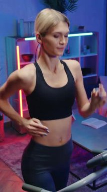 Sağlıklı ve sportif yaşam tarzı konsepti. Güzel, kendine güveni tam atletik, narin, 25 yaşında, spor kıyafetli sarışın gece arkaplanda koşan bir makinede koşuyor.