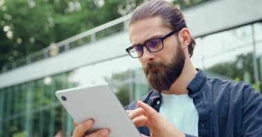 Modern bir ofis binasının yakınında dikilirken tablet üzerindeki finansal verileri analiz eden odaklanmış işadamını kapatın. Modern iş, dijital teknoloji ve kurumsal iletişim kavramı