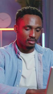 Sempatik, başarılı, 30 yaşında, siyah tenli, güzel dekore edilmiş ev ofisinde daktilo eden, kameraya gece aydınlatmalı, samimi bir gülümsemeyle poz veren bir adam.