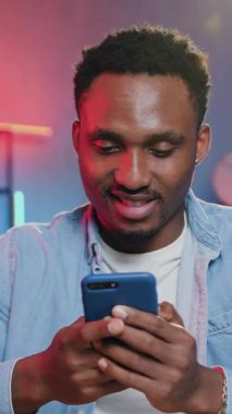 Çekici, pozitif, rahat, Afro-Amerikan gençliği. Akıllı telefondaki sosyal medya bilgilerini gözden geçiriyor. Evdeki, öndeki bilgisayardaki fazla mesai çalışmasında mola veriyor.