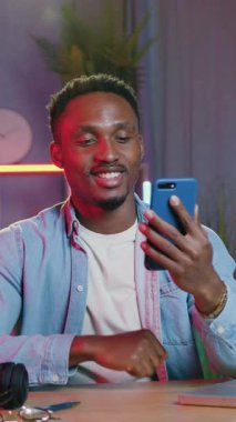 Modern teknoloji konsepti. Sevimli, neşeli, kaygısız, 30 yaşındaki Afrikalı Amerikalının, evdeki ofiste, arkadaşlarıyla ya da aileleriyle video sohbetleri yoluyla oturup sohbet ettiği yer.