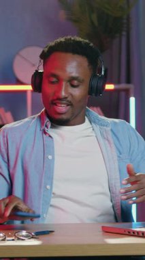 Memnuniyetle eğlendirici, gülümseyen 30 yaşındaki Afro-Amerikan işyerinde gece lambası efektleriyle oturuyor ve dans eden kulaklıklarda en sevdiği şarkıları dinliyor.