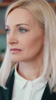 Good-looking dreamy successful light haired female office manager posing on camera on well-equipped office room background with sincerely smile,front view