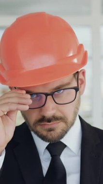 İyi görünümlü, yetenekli, stil sahibi, gözlüklü ve kasklı bir mimar. Kapalı bir ofiste ya da inşaat alanında kamera önünde poz veriyor.