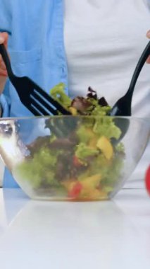 Taze sağlıklı salatayı marul, biber ve domatesle hazırlayan ve aile yemeğinde şeffaf kâsede karıştıran kadın elleri.