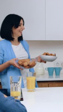 İyi görünümlü, neşeli baba ve iki oğlu mutfak masasının yanında aile kahvaltısı yaparken siyah saçlı anne iki kâseyi lezzetli bisküvilerle kaplıyor.