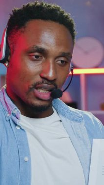 Uzaktan kumandalı iş konsepti. Kulaklıklarda, mikrofonla müşterilerle görüntülü konuşma yapan ve iş stratejisi hakkında konuşan yakışıklı, konsantre, genç, Afro-Amerikan yönetici.